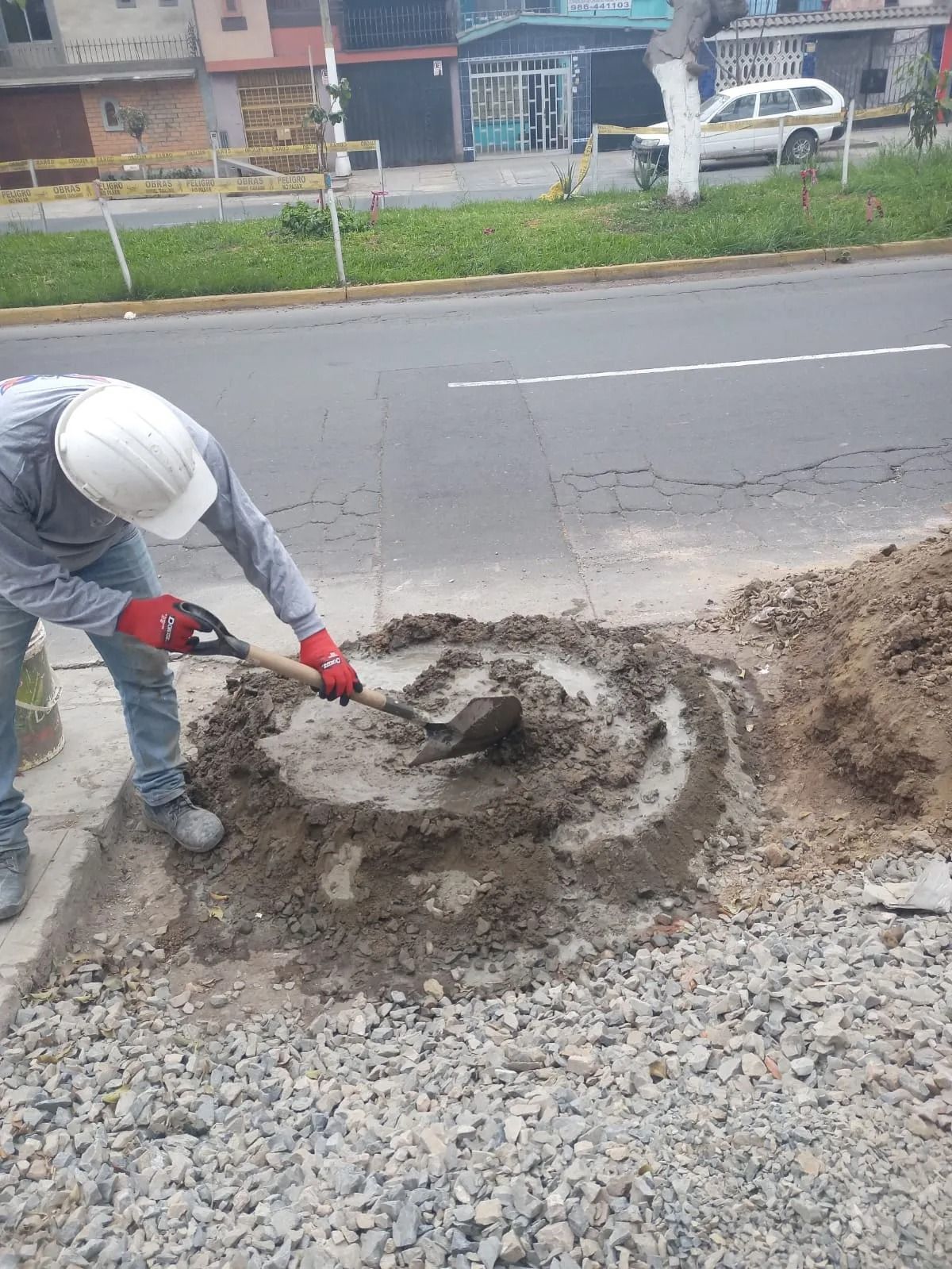 Obrero con casco blanco paleando grava junto a una zona en construcción de la carretera.