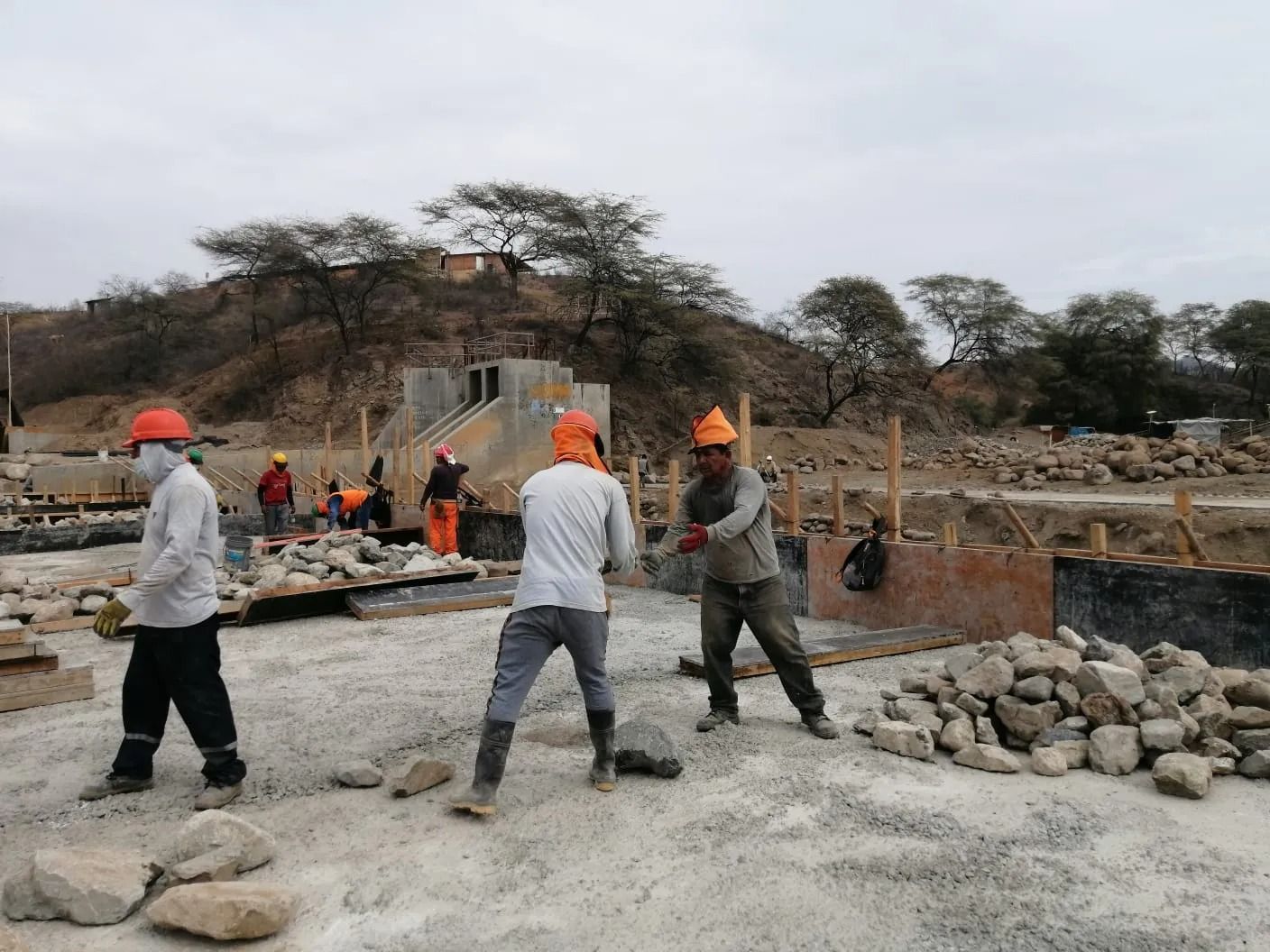 Obreros de la construcción con cascos naranjas pavimentan con hormigón en un sitio al aire libre 