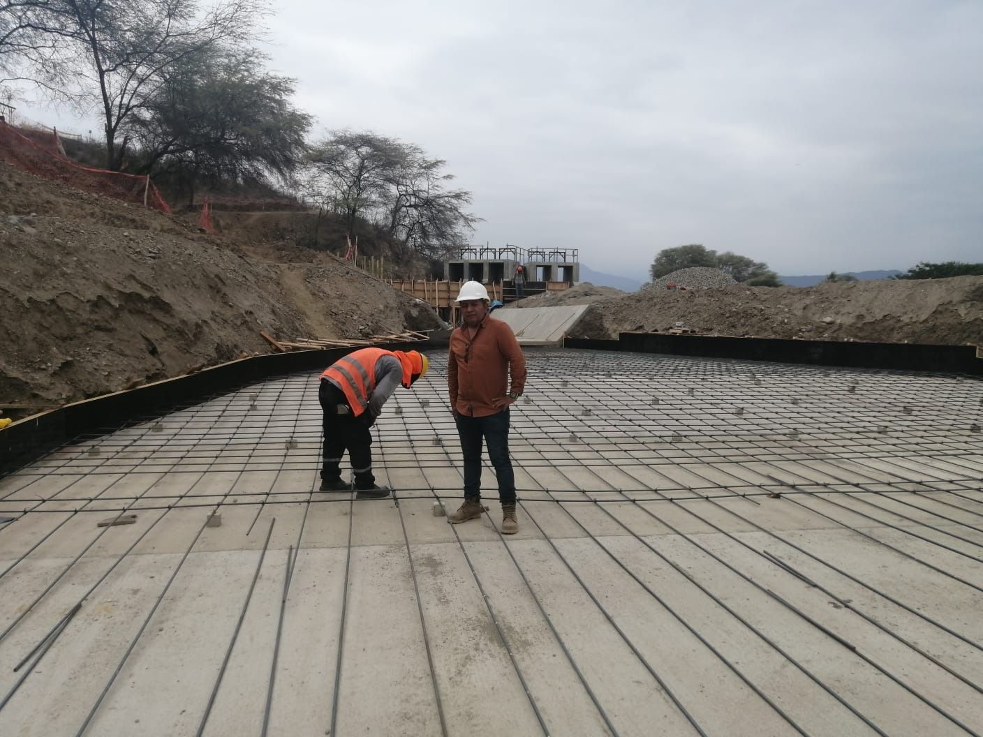 Dos trabajadores en una obra de construcción de hormigón, uno agachado cerca de las barras de refuerzo