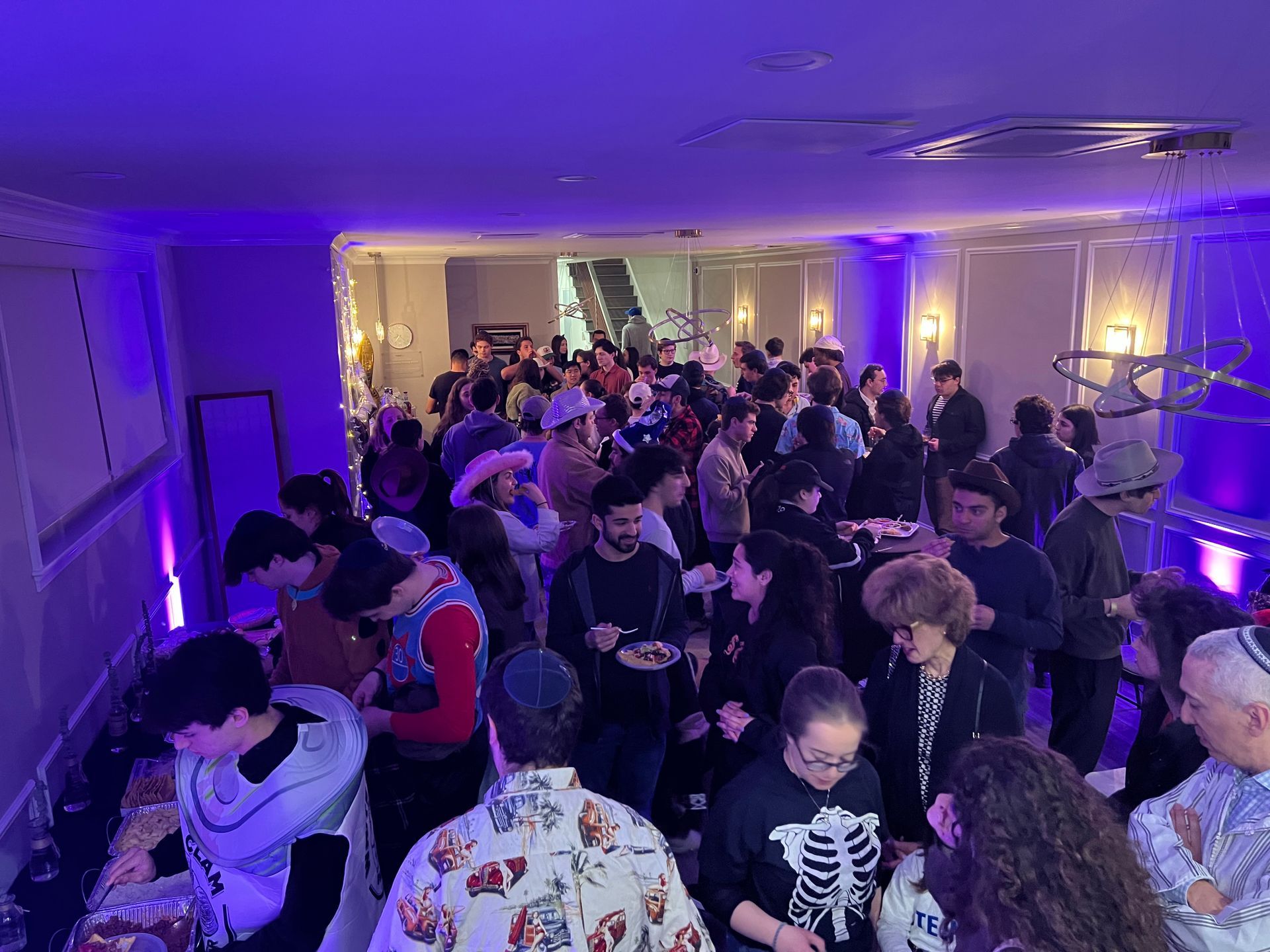 a large group of people are standing in a room with purple lights .