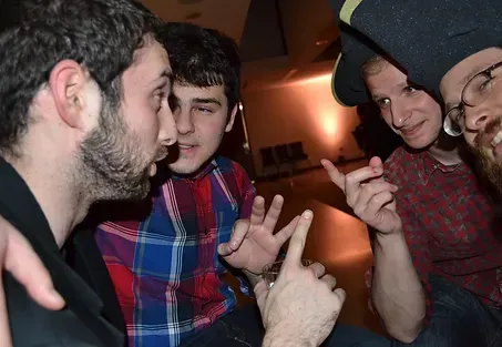A group of young men are sitting around a table making funny faces.