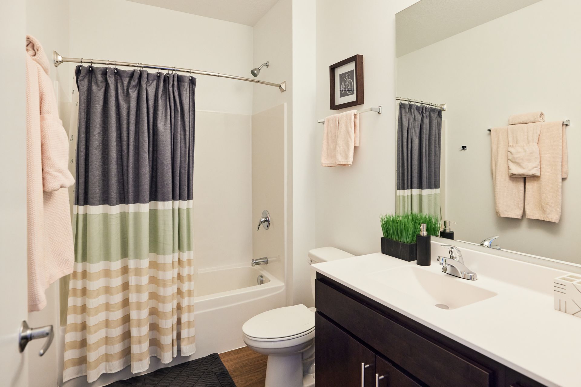 Bathroom with dark brown vanity, white countertop, shower with patterned curtain, and mirror at Southsider Apartments in Minneapolis, MN.