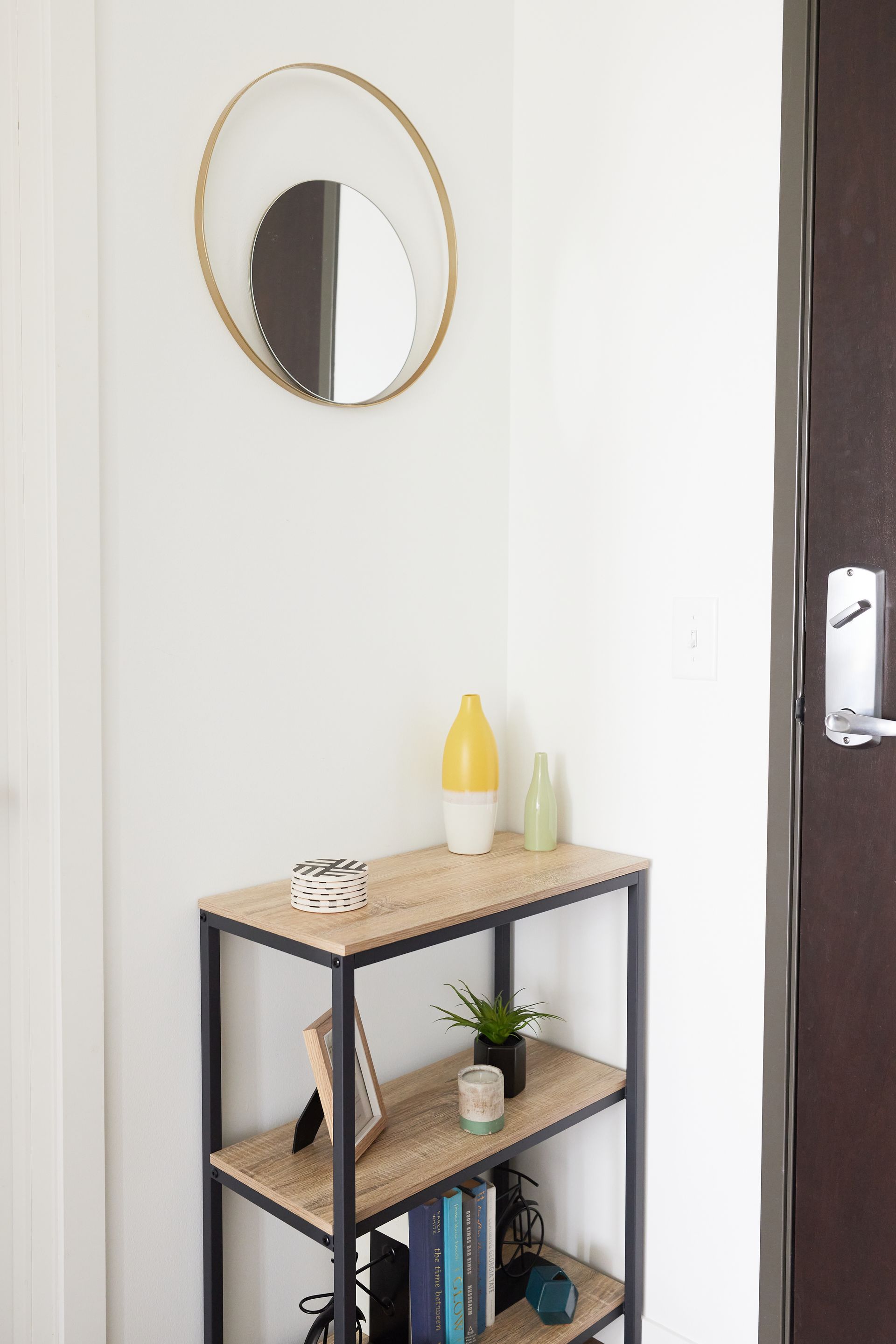 A small entryway with a shelf holding decor, a circular mirror, and a brown door at Southsider Apartments in Minneapolis, MN.