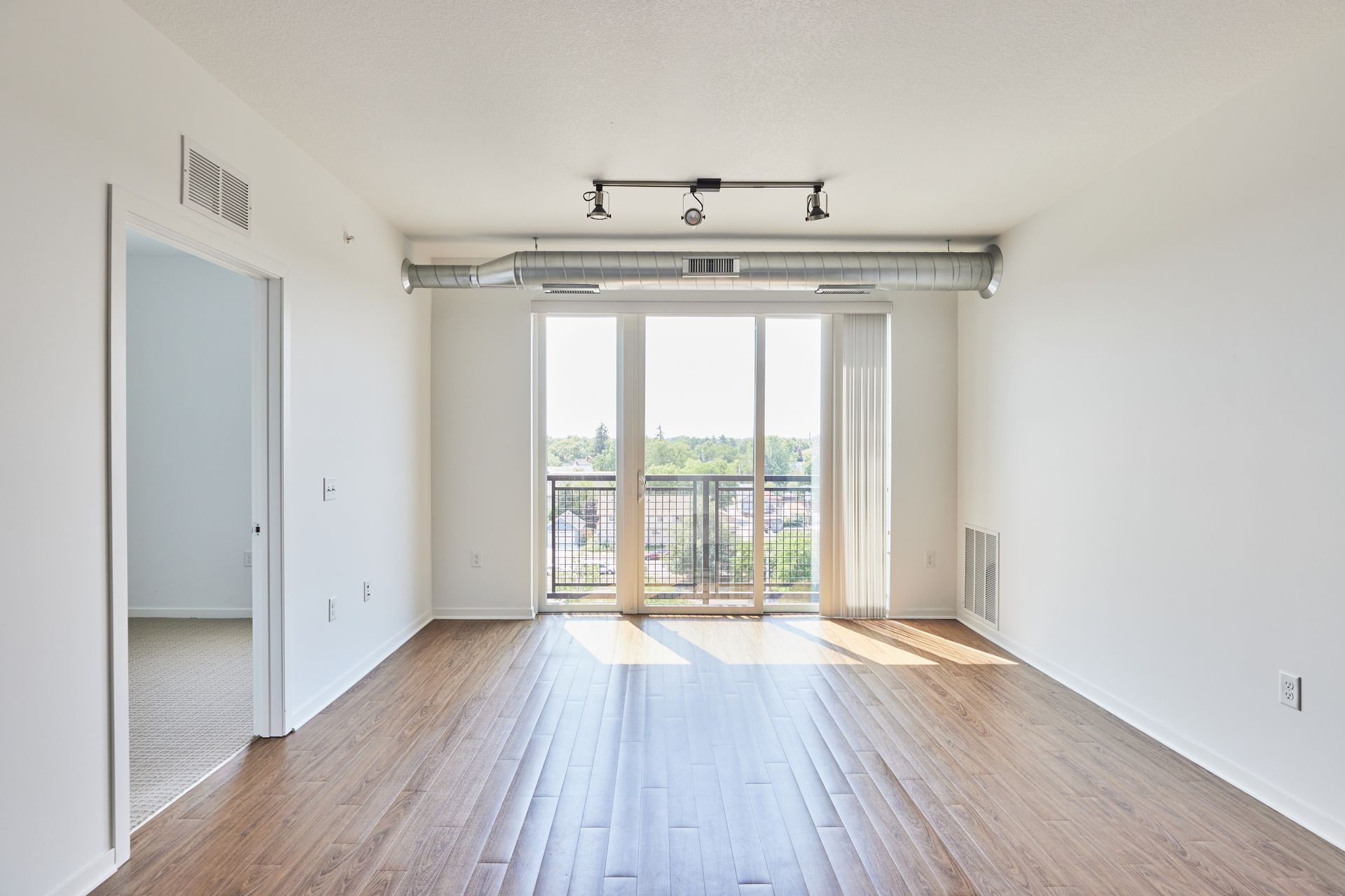 Empty living room with wood floors, large windows, and a balcony at Southsider Apartments in Minneapolis, MN.