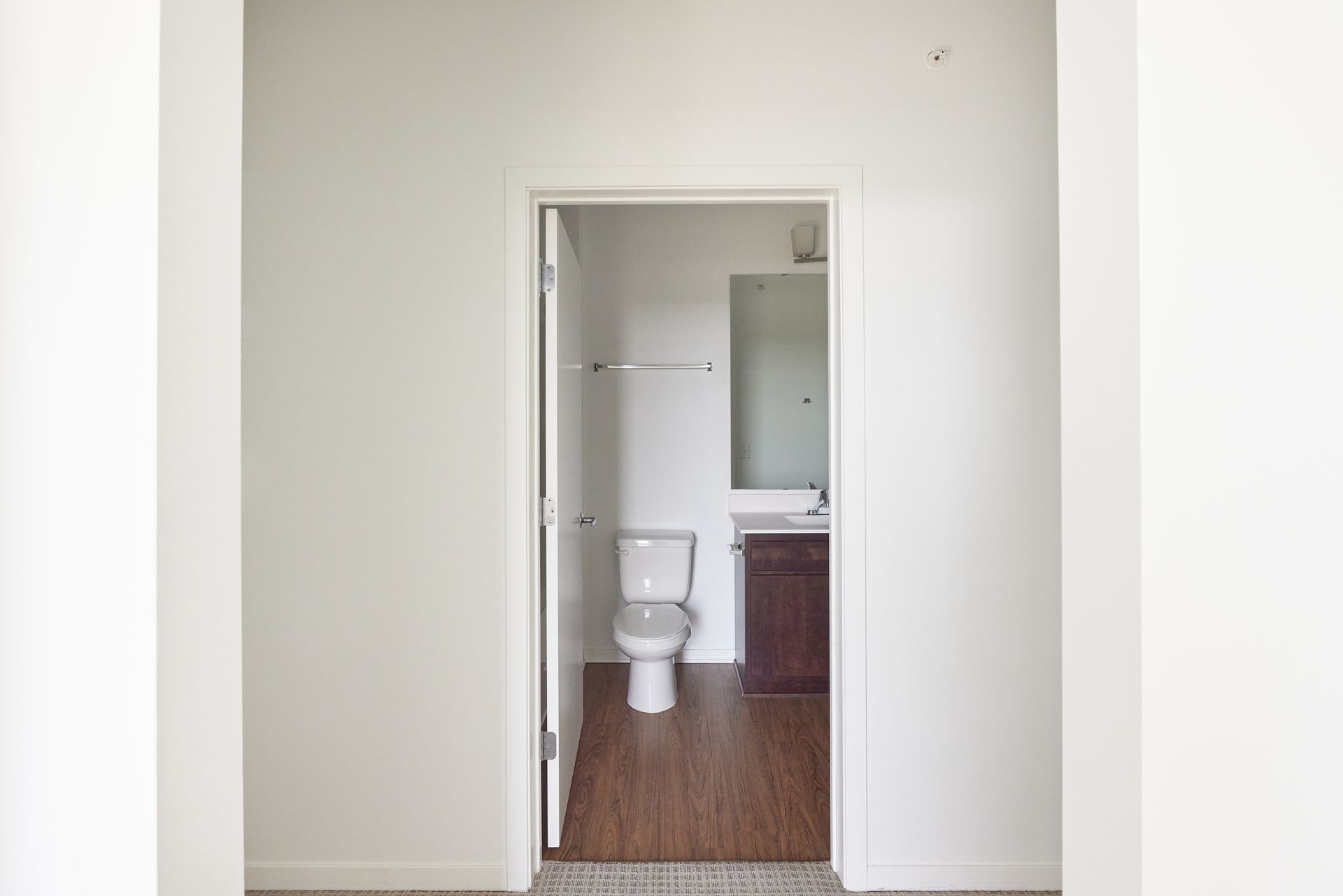 Open doorway to a bathroom with a toilet, mirror, and vanity; hardwood floors at Southsider Apartments in Minneapolis, MN.