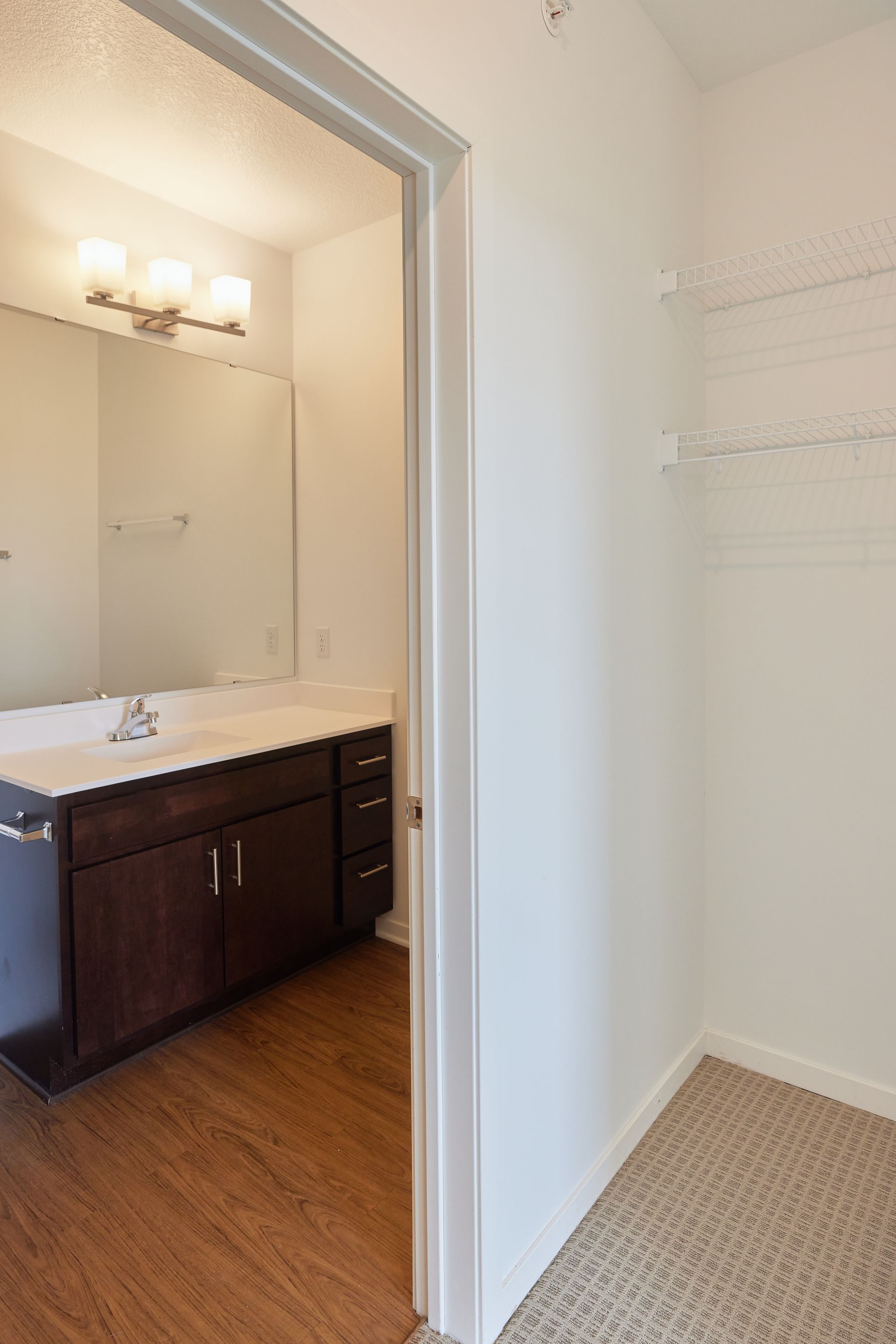 Open doorway to bathroom, view of vanity and mirror. Closet with wire shelving on the right at Southsider Apartments in Minneapolis, MN.