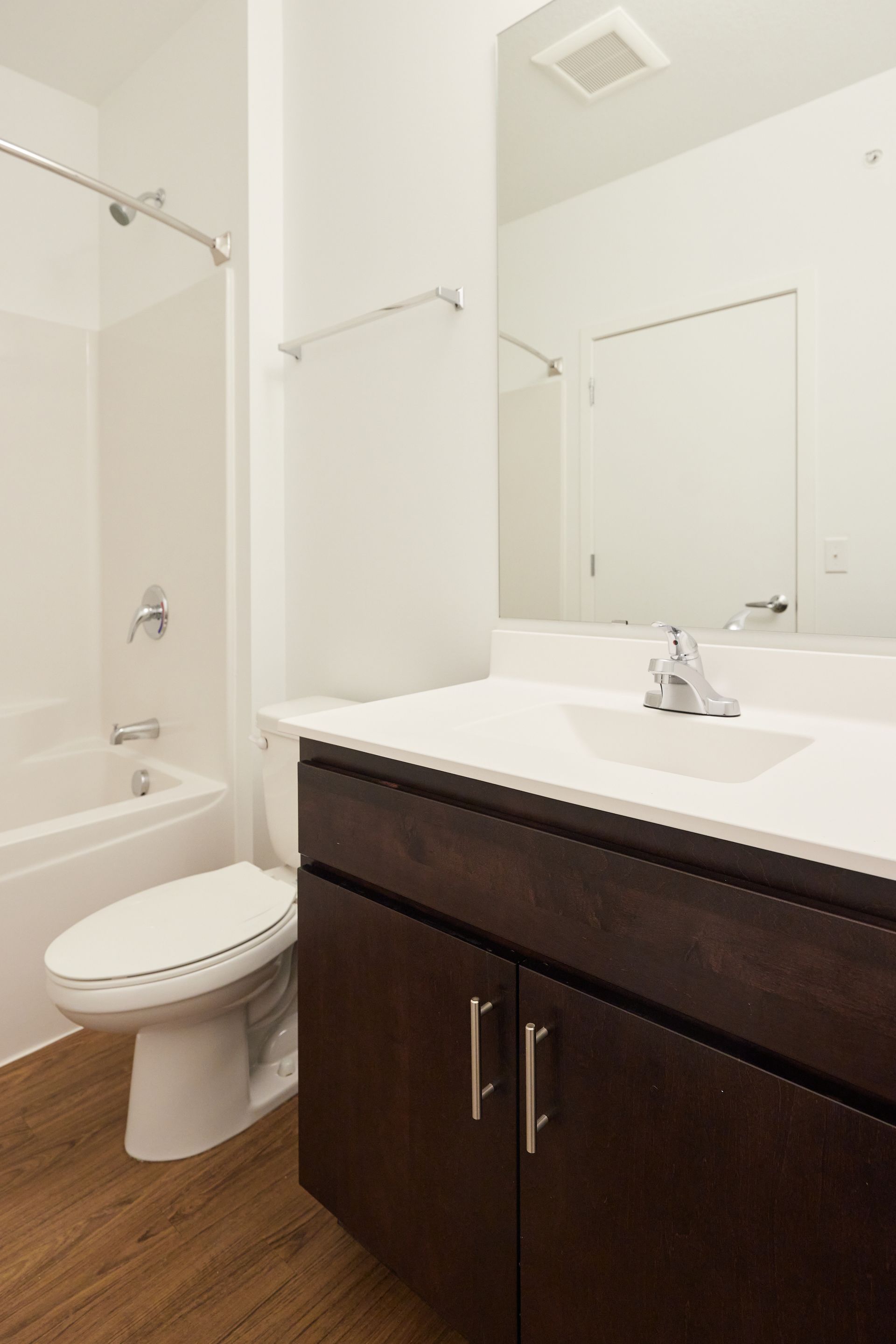 Bathroom with white walls, brown vanity, white toilet, and shower/tub combo at Southsider Apartments in Minneapolis, MN.
