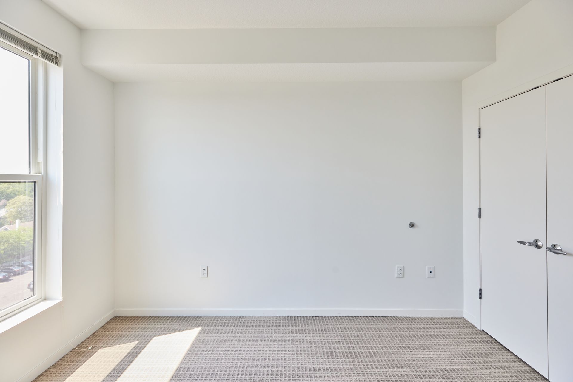 Empty white room with a window, door, and light-colored carpet at Southsider Apartments in Minneapolis, MN.