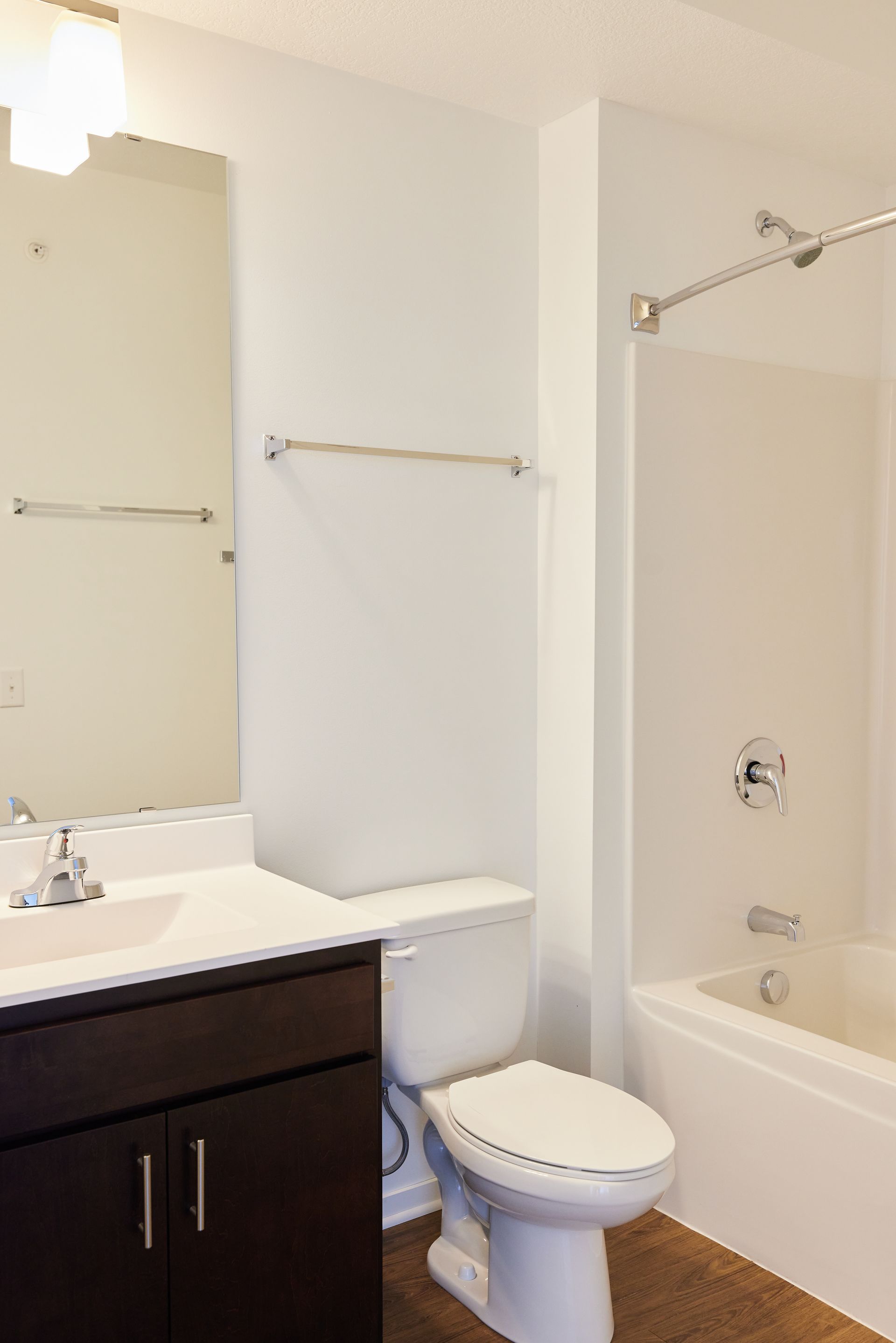 Bathroom with a toilet, sink, mirror, and bathtub. White walls and a dark brown cabinet at Southsider Apartments in Minneapolis, MN.