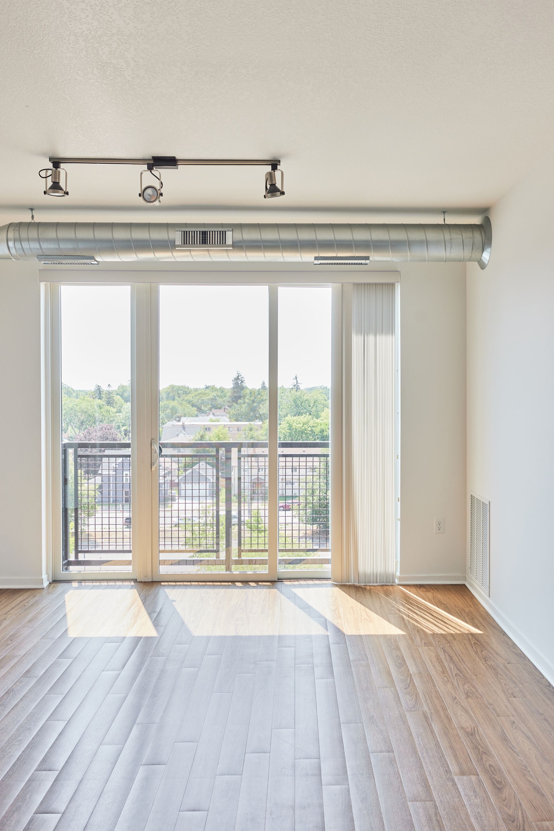 Empty sunlit room with balcony access, hardwood floors, and exposed ductwork at Southsider Apartments in Minneapolis, MN.