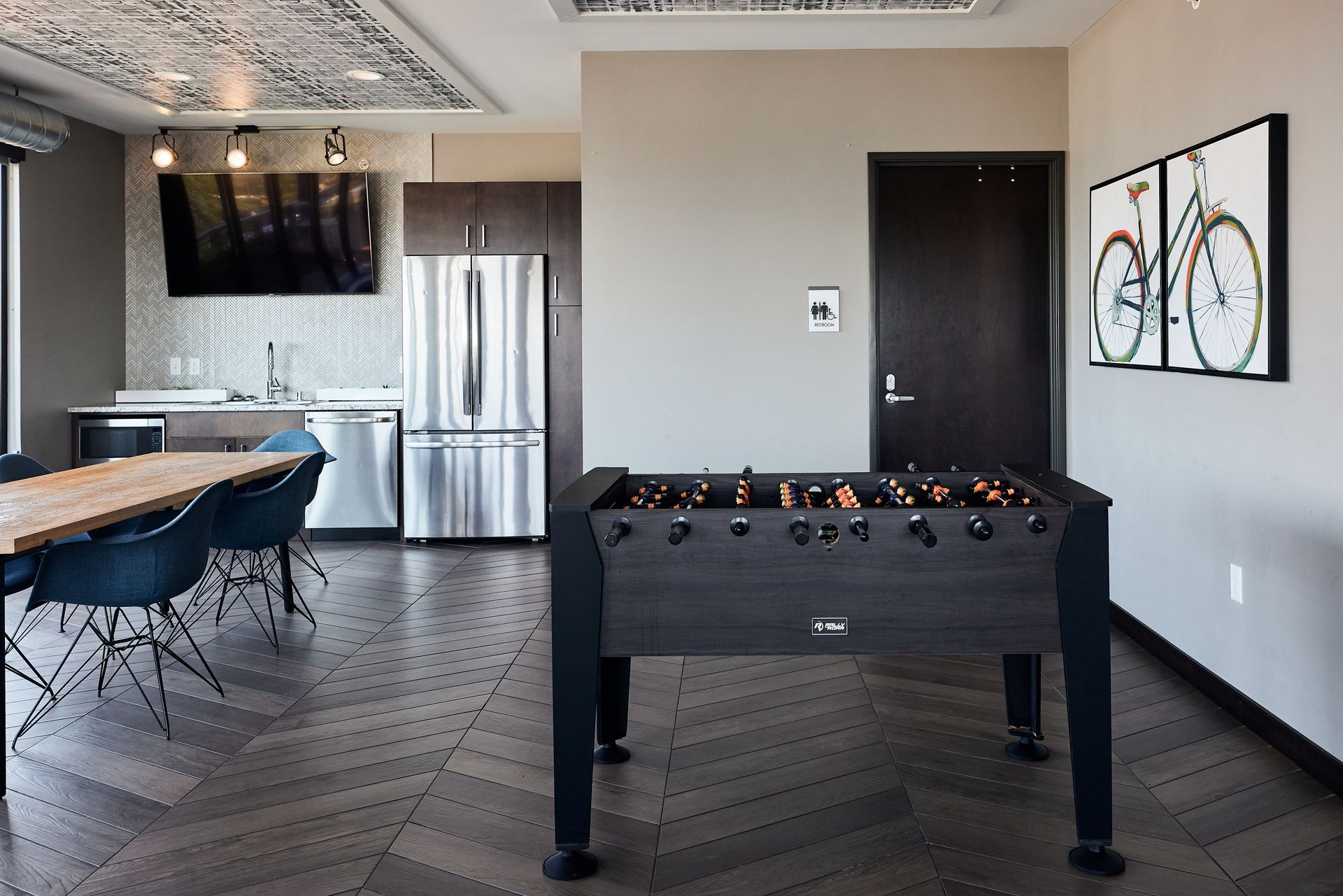 Foosball table in a modern lounge with a dining table, kitchen, and bicycle art at Southsider Apartments in Minneapolis, MN.