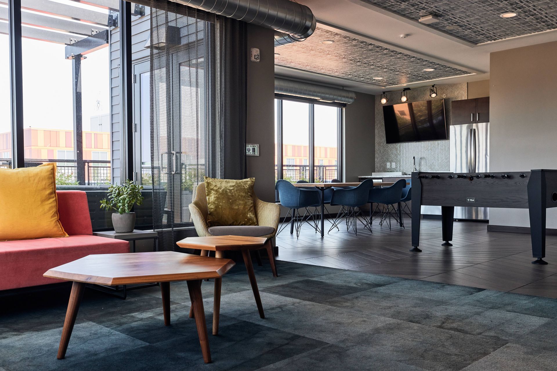 Modern lounge area with seating, foosball, kitchen, and large windows at Southsider Apartments in Minneapolis, MN.