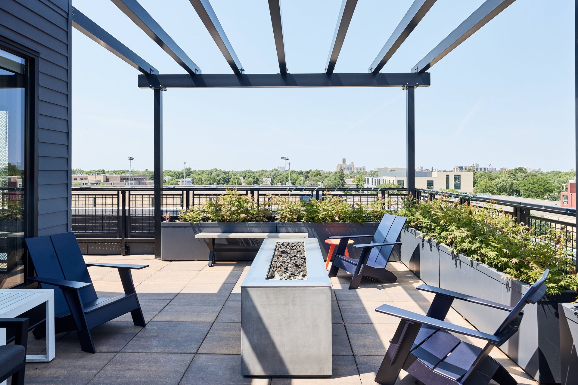 Rooftop patio with modern furniture, fire pit, and pergola overlooking cityscape on a sunny day at Southsider Apartments in Minneapolis, MN.