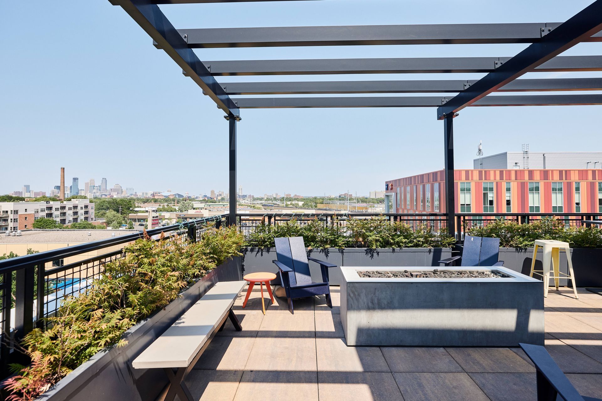 Rooftop patio with seating, a fire pit, and city view on a sunny day at Southsider Apartments in Minneapolis, MN.