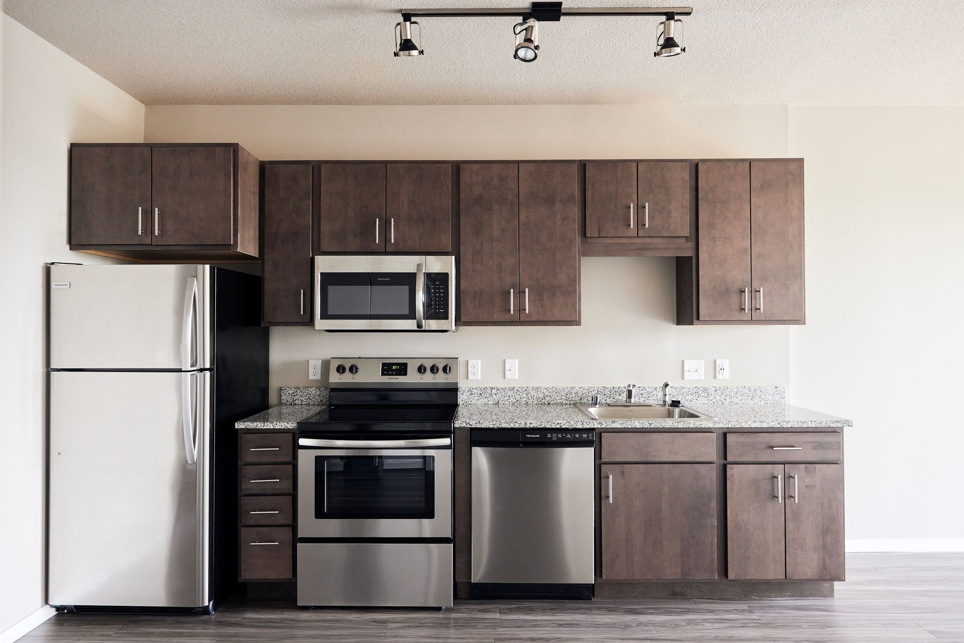 A modern kitchen with stainless steel appliances, brown cabinets, and a granite countertop at Southsider Apartments in Minneapolis, MN.