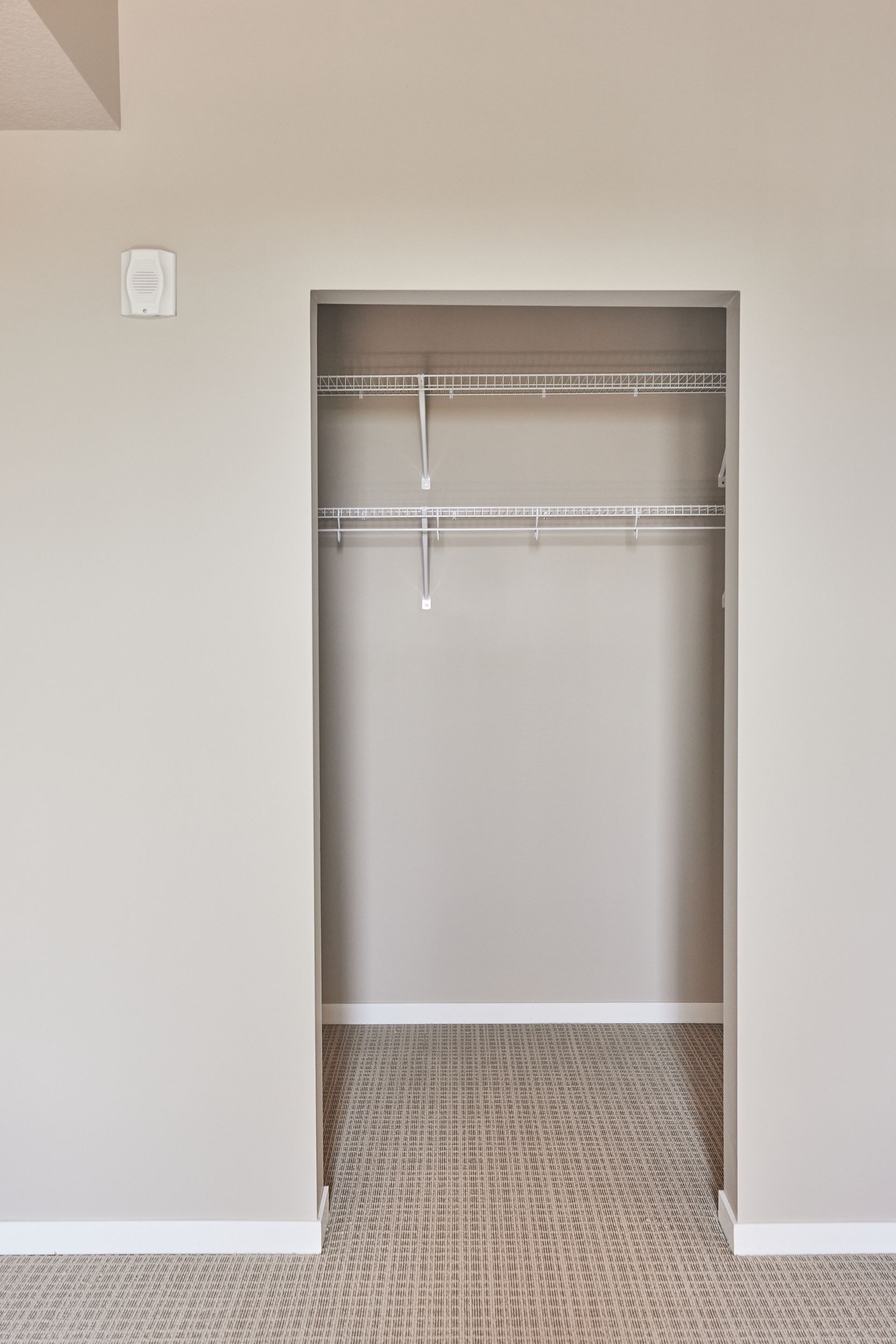 Empty walk-in closet with wire shelving and carpeted floor, beige walls at Southsider Apartments in Minneapolis, MN.