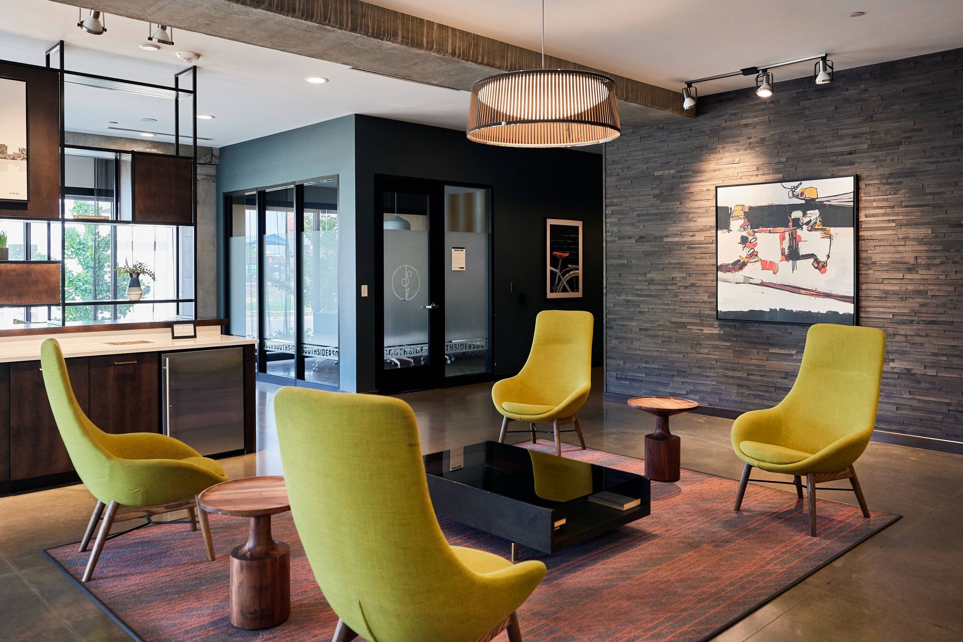 Lounge area with yellow chairs, a black coffee table, and abstract art on a gray brick wall at Southsider Apartments in Minneapolis, MN.