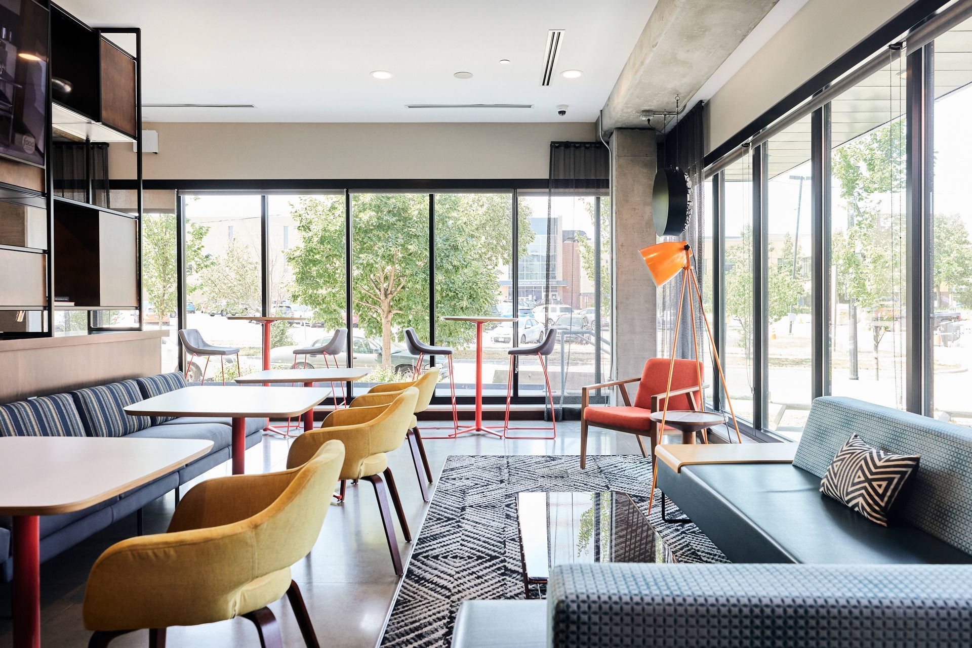 Modern cafe interior with floor-to-ceiling windows, seating in various colors and styles, and a view of outside trees at Southsider Apartments in Minneapolis, MN.