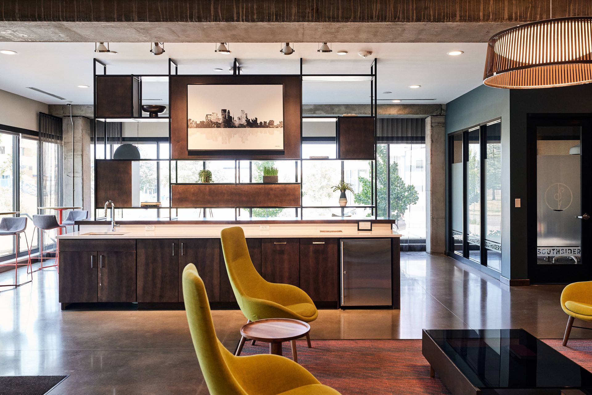 Modern open-concept space with yellow chairs, dark wood cabinets, and an open shelving unit at Southsider Apartments in Minneapolis, MN.