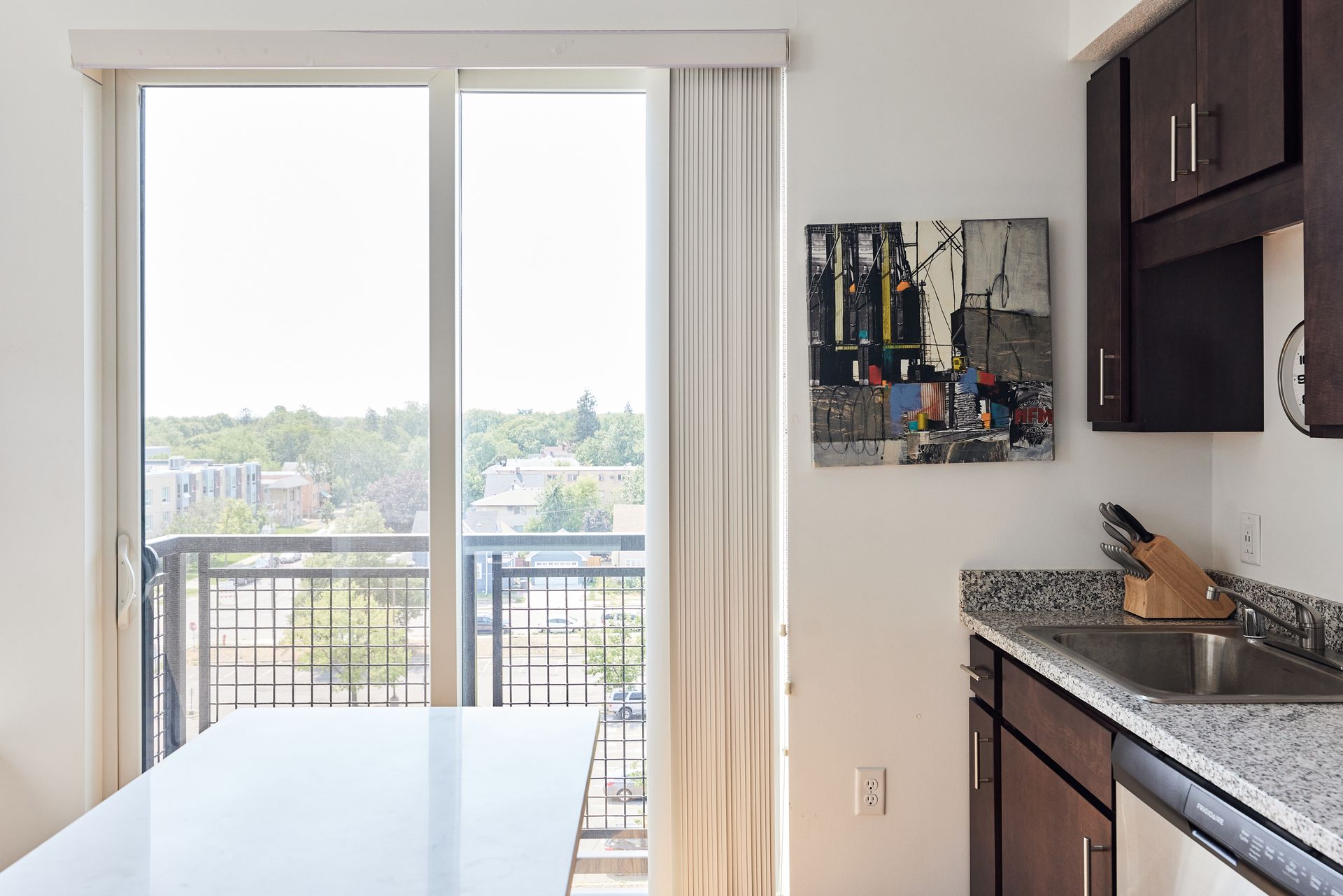Kitchen with balcony access and cityscape view. Features dark cabinets, artwork, and a white table at Southsider Apartments in Minneapolis, MN.
