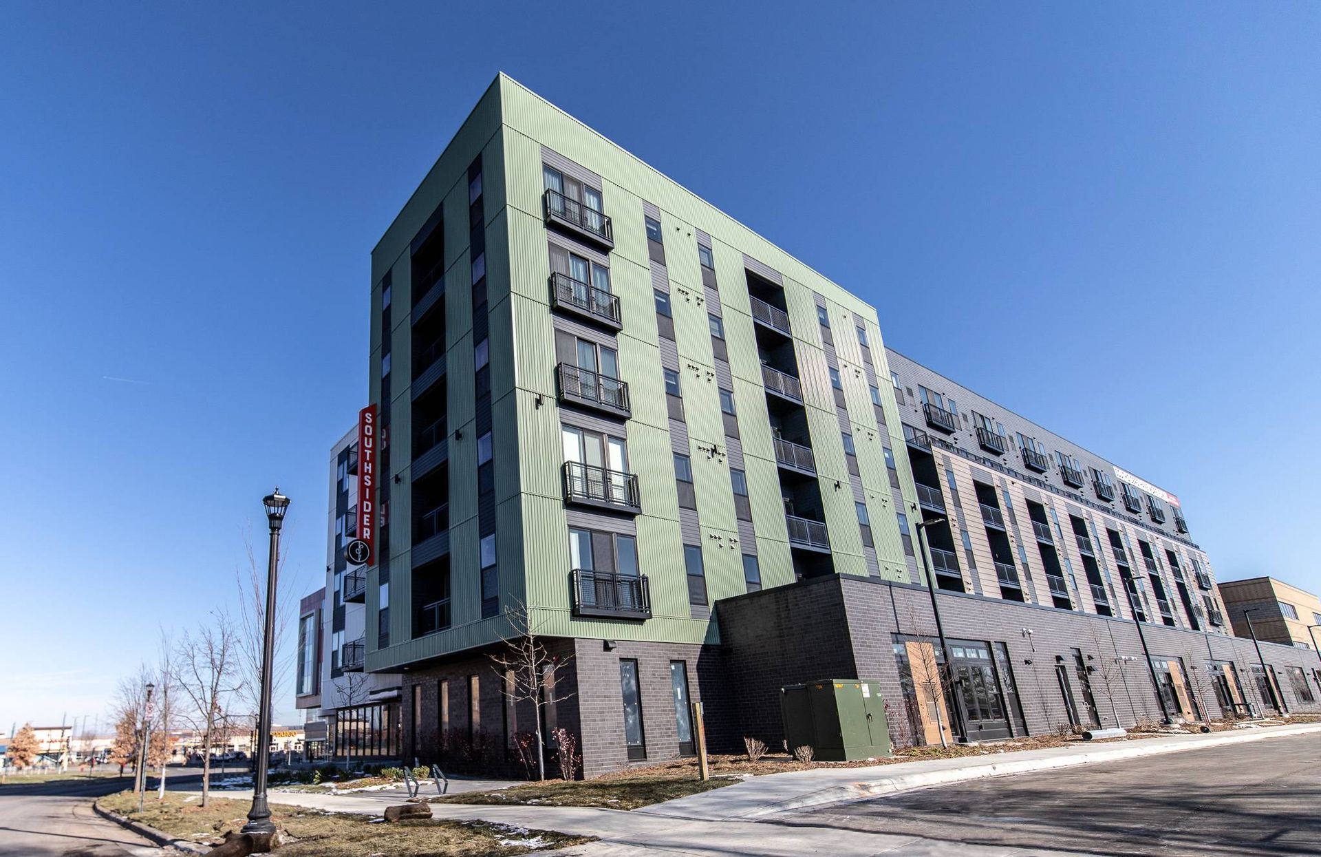Multi-story modern building with green and black facade against a blue sky at Southsider Apartments in Minneapolis, MN.