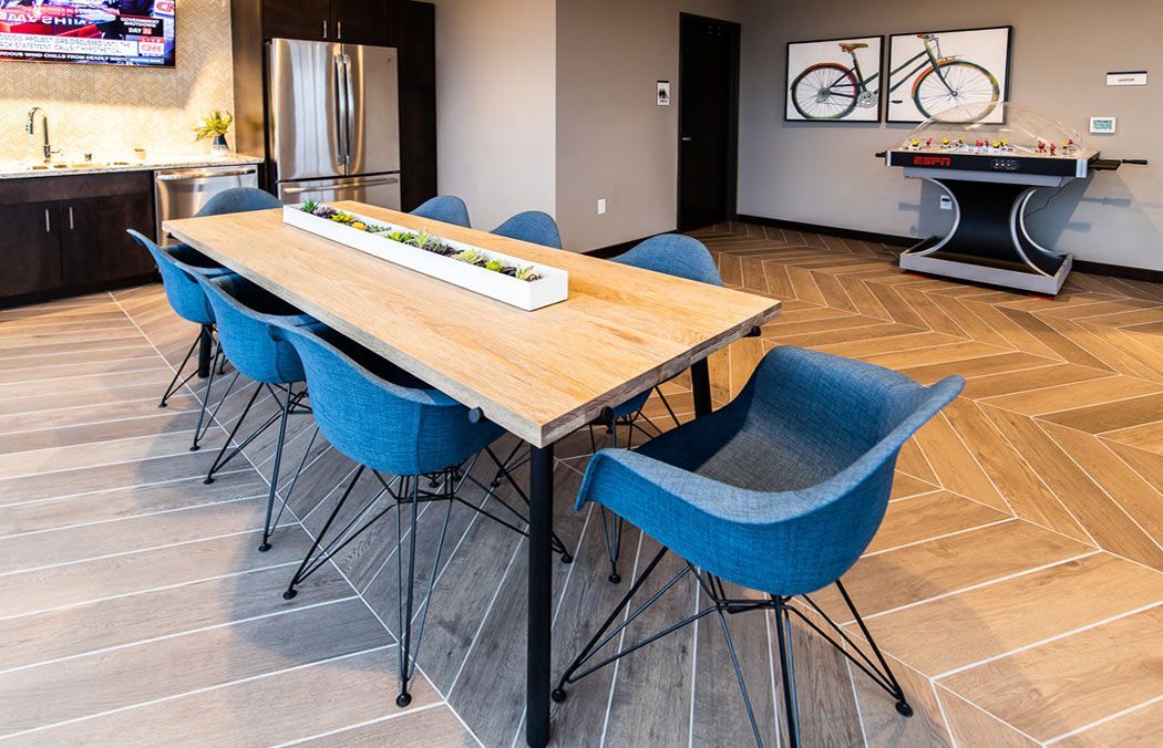 Long wooden table with blue chairs in a room with a foosball table and art at Southsider Apartments in Minneapolis, MN.