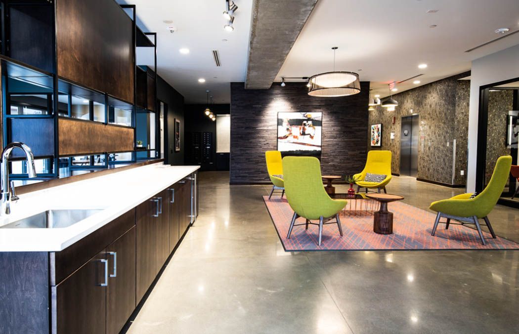Modern lounge with lime green chairs, a pink rug, and a dark wood accent wall at Southsider Apartments in Minneapolis, MN.