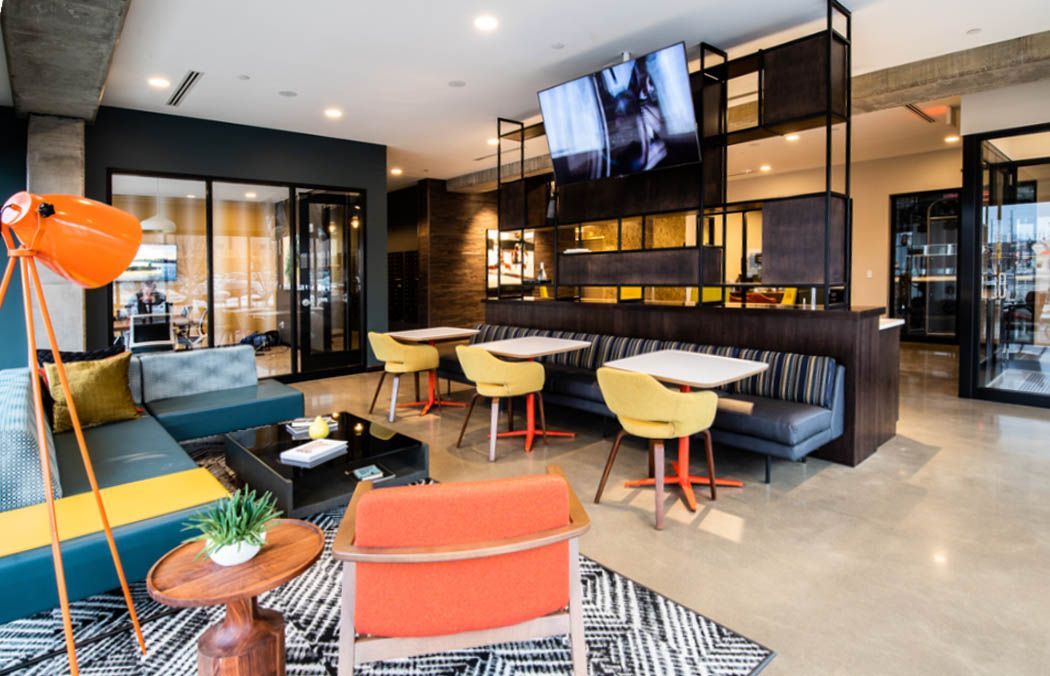 Modern lounge with seating, tables, tv, and orange accents; a social gathering space at Southsider Apartments in Minneapolis, MN.