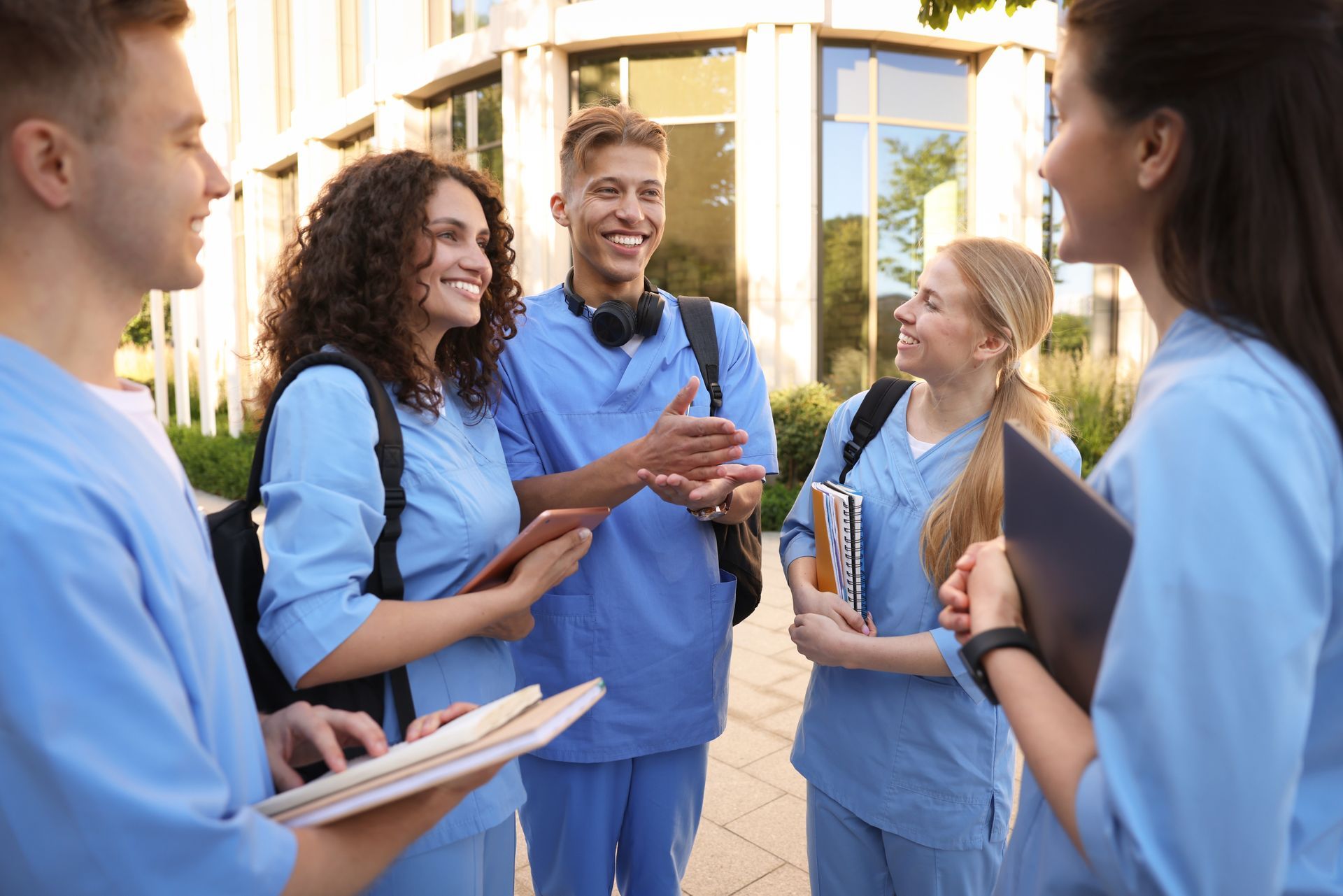 Group of medical staff in blue scrubs talking and smiling outside a building