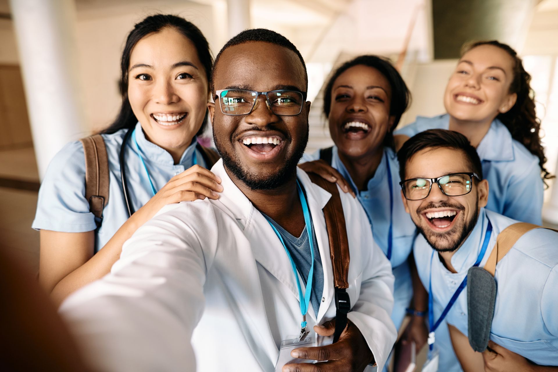 Smiling team in blue scrubs taking a selfie in a bright hospital hallway