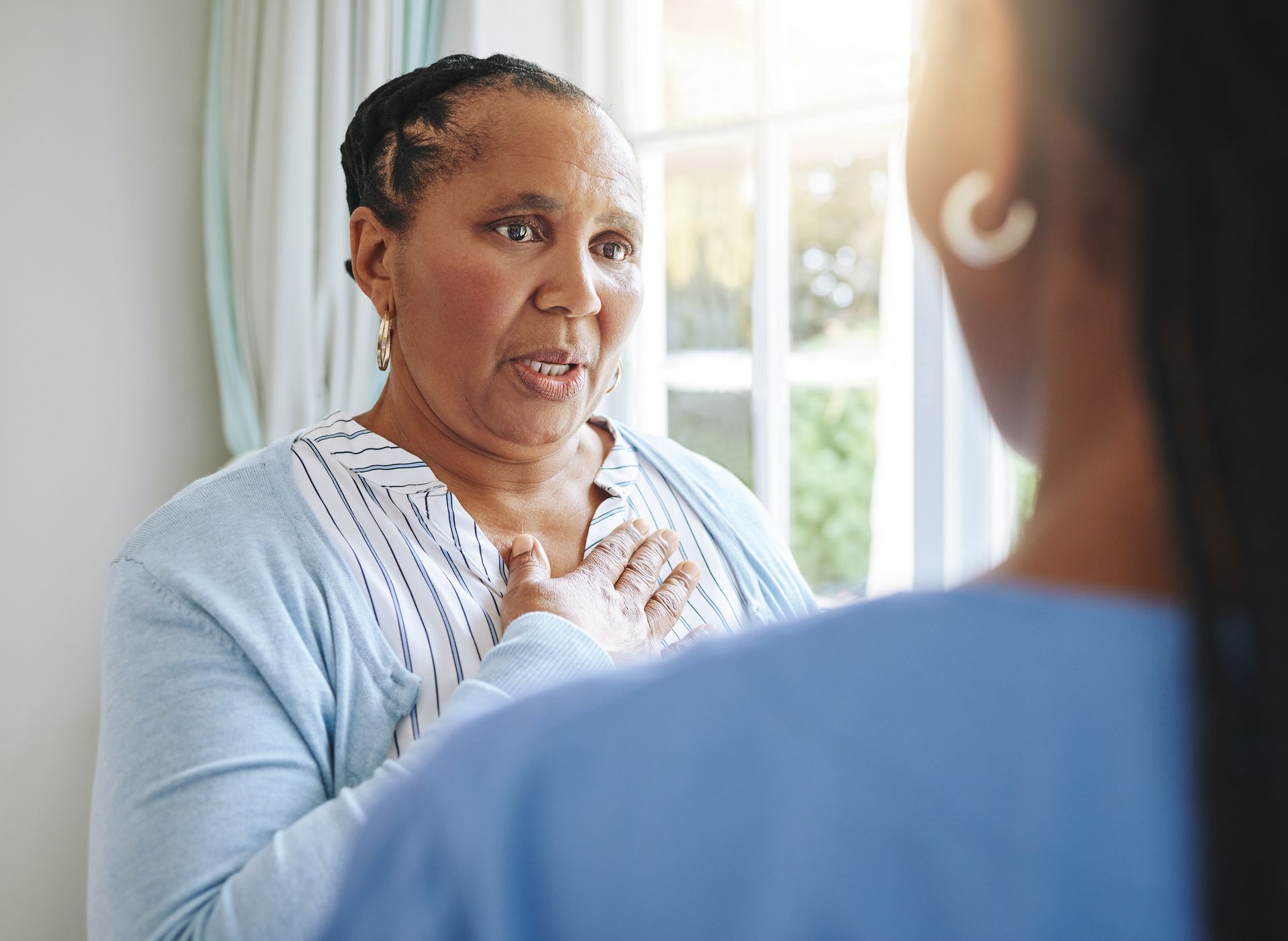 Woman speaking with a clinician in a bright room, hand on chest, during a conversation.