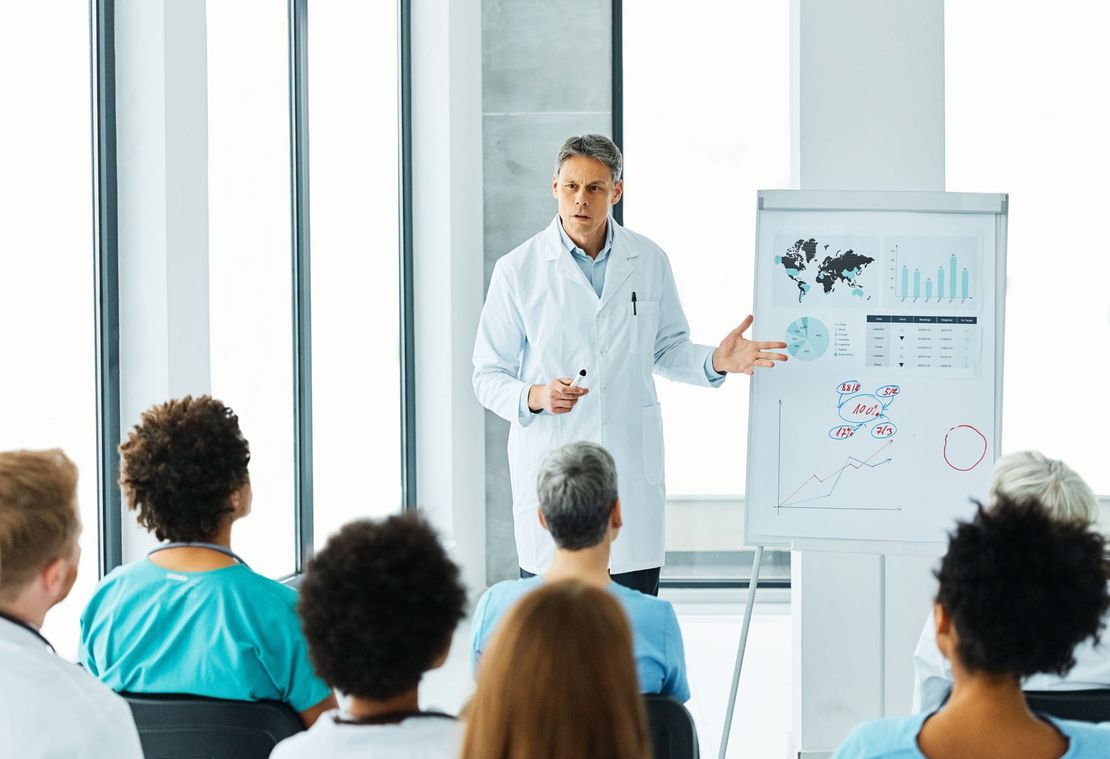 Presenter giving a talk to seated audience beside a flip chart in a bright meeting room