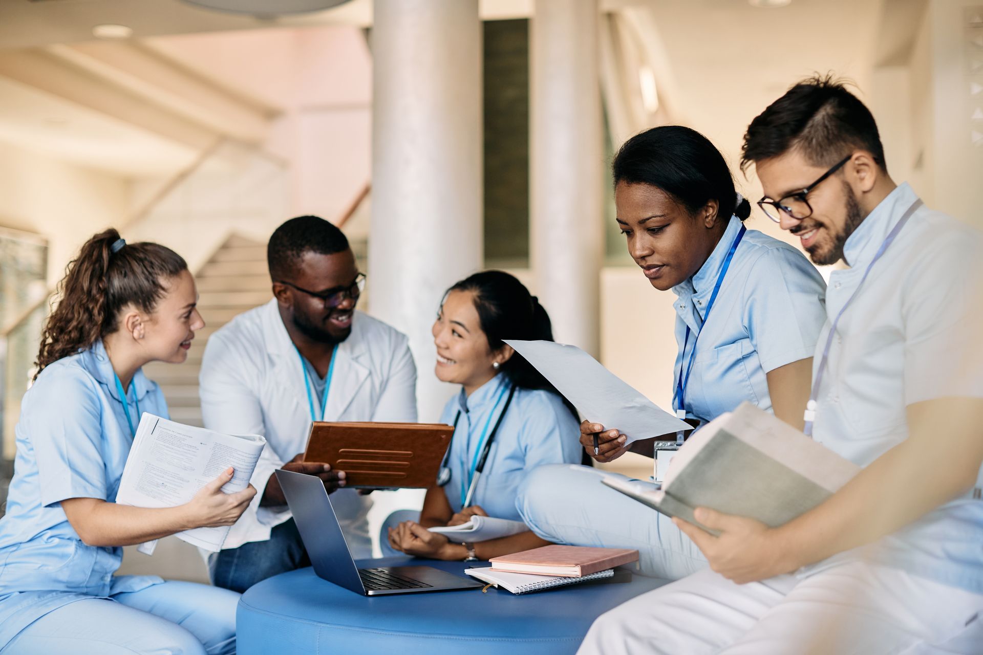 Group of medical professionals collaborating around a laptop in a bright hospital lounge