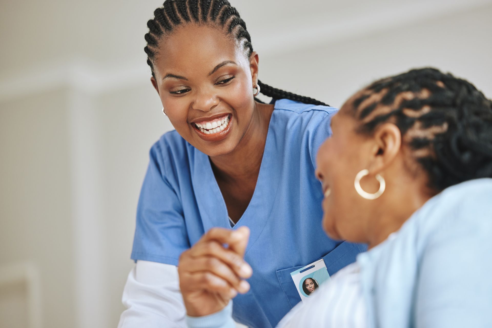 Two healthcare workers in blue scrubs smiling and talking in a clinical setting
