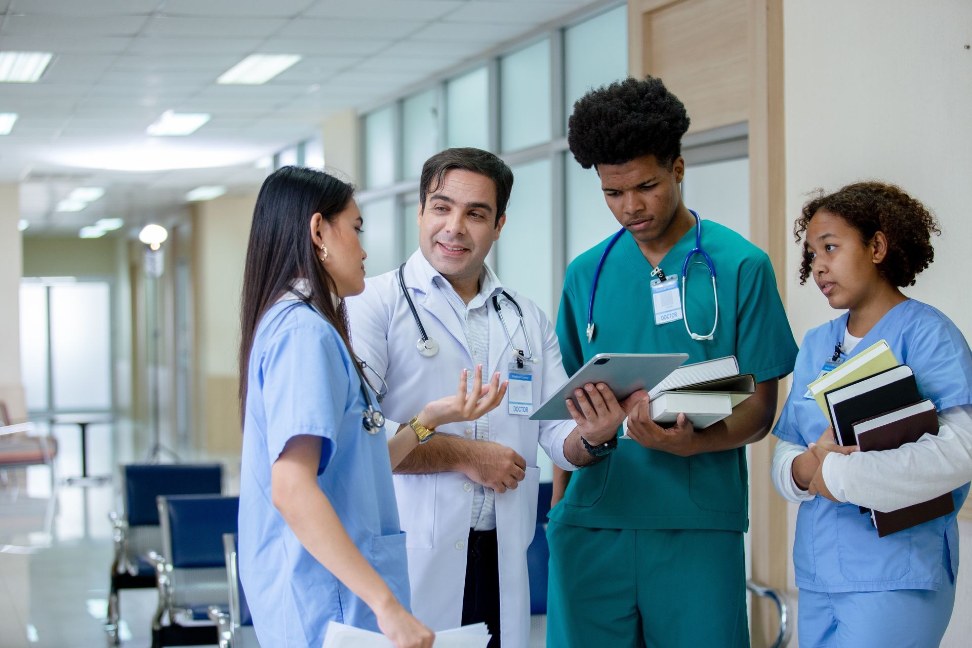 Healthcare worker in blue scrubs holding a clipboard in a hospital corridor