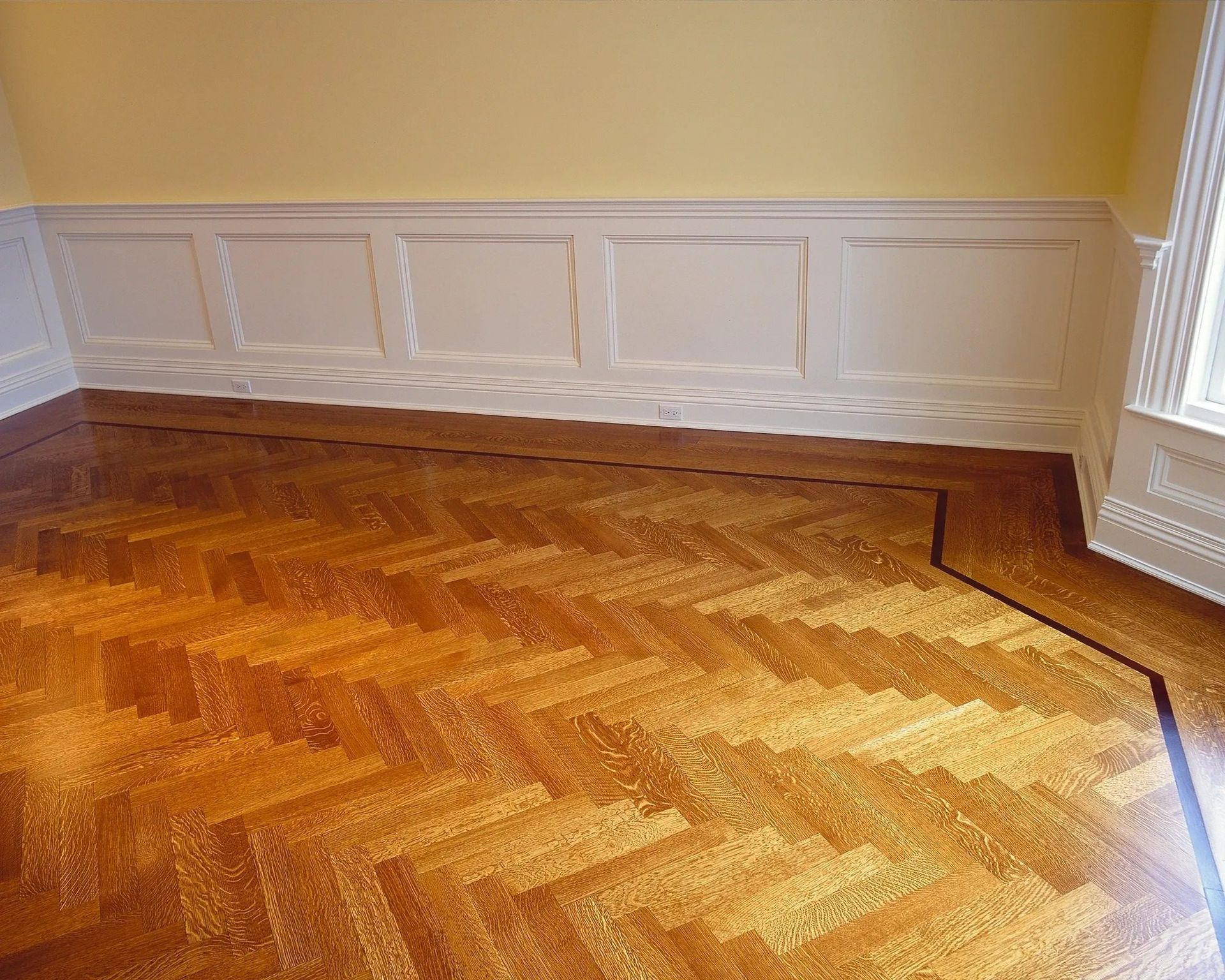 Empty room with herringbone hardwood floor, white paneled walls, and yellow walls above trim.