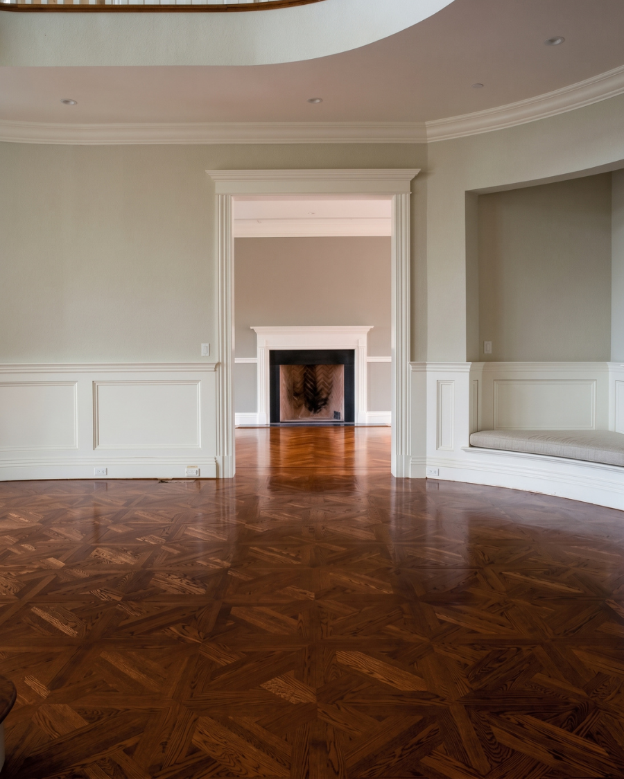 Empty elegant living room with polished wood floor, cream walls, and a fireplace centered on the far wall