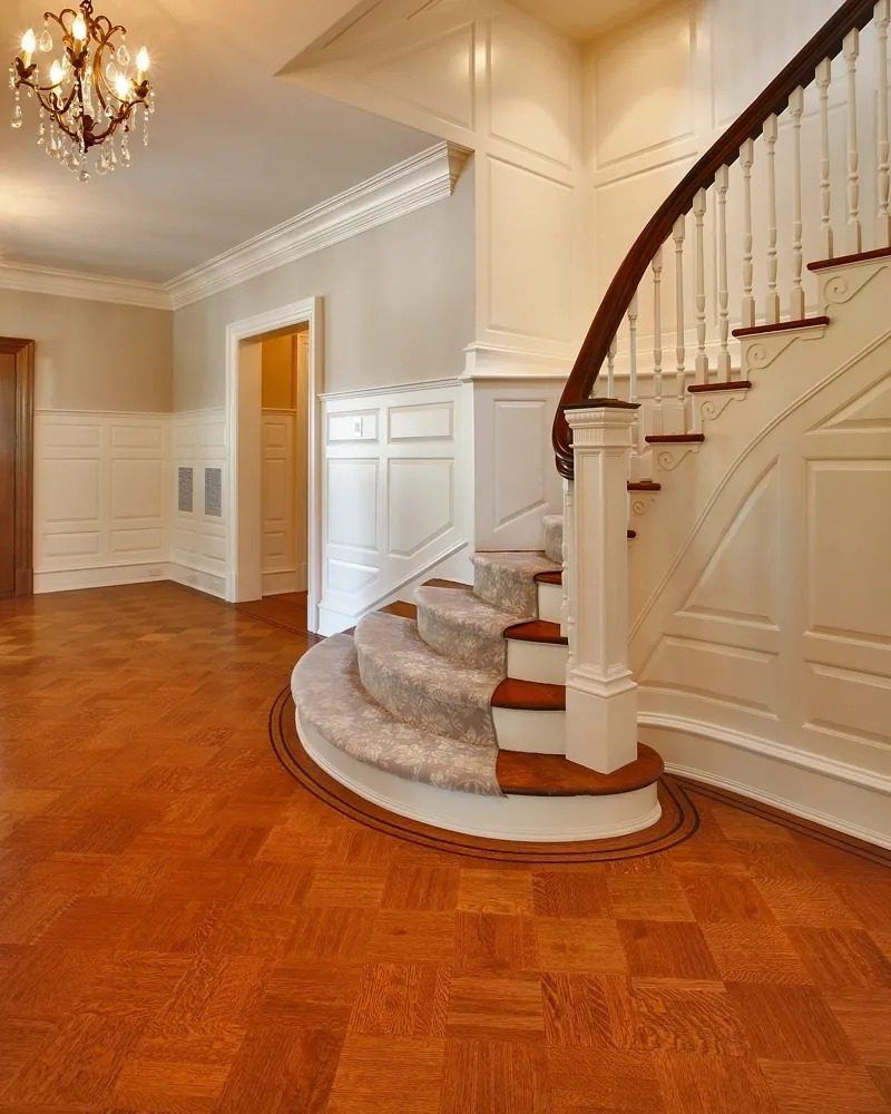 Elegant foyer with curved carpeted staircase, hardwood floor, white paneled walls, and chandelier
