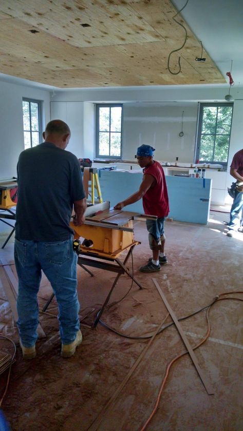 People working in an unfinished room with exposed wiring, tools, and construction materials.