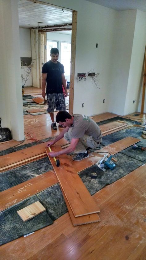 Workers installing wood flooring in a room under renovation, with planks and tools on the floor.