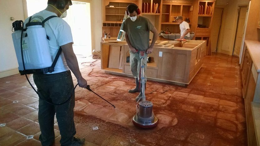 Two workers operating floor buffers in a room with wood cabinets and a polished stone floor