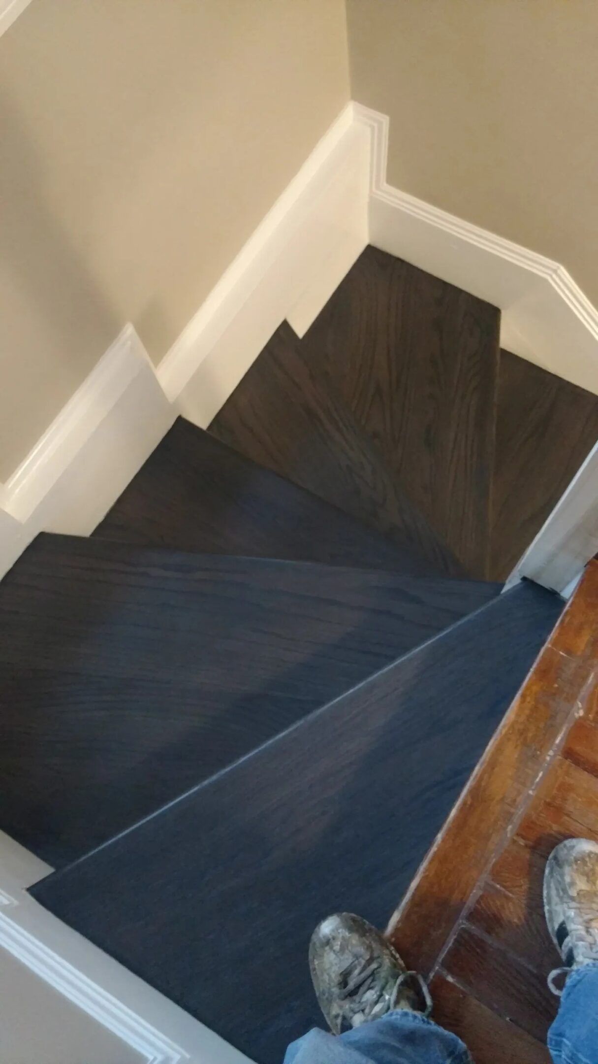 Spiral staircase with dark carpet and white walls, viewed from the top down.