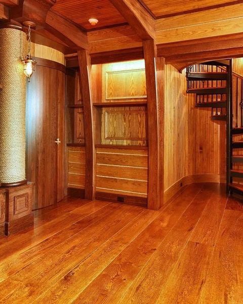 Warm wooden hallway with polished floors, paneled walls, built-in shelving, and a spiral staircase.