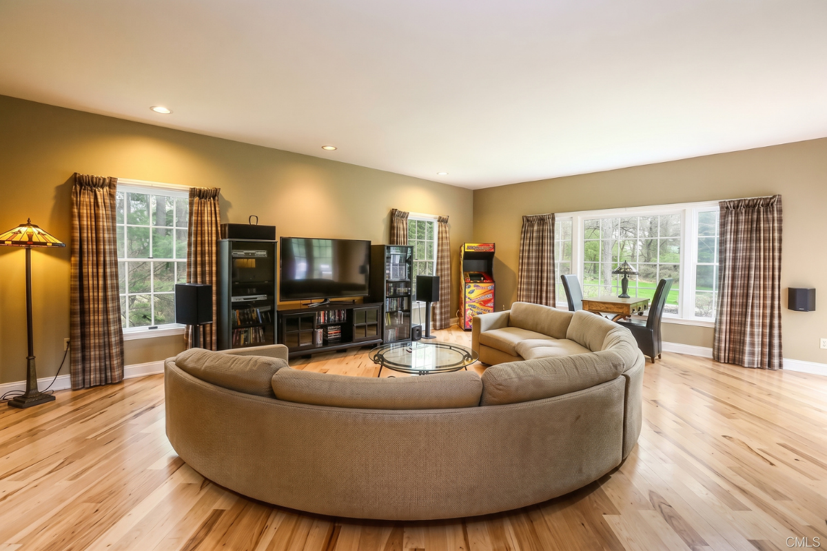 Spacious living room with curved sofa, TV, floor lamp, and large windows letting in natural light