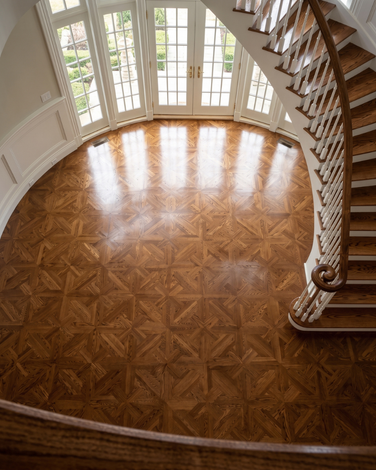 Elegant staircase and polished parquet floor in a bright foyer with tall windows