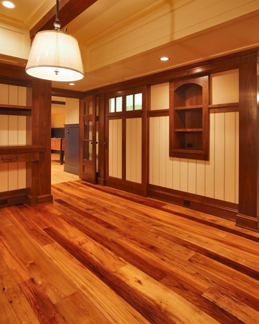 Empty wooden room with polished hardwood floors, built-in shelves, and hanging lights