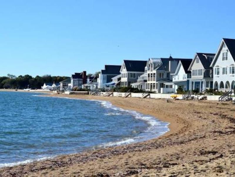 Sandy beach with calm water and a row of white seaside houses under a clear blue sky