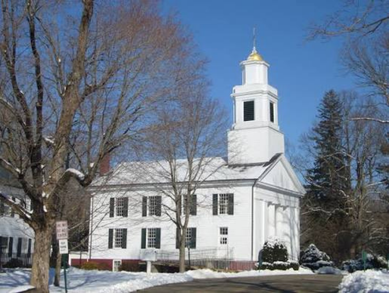 White church with gold steeple in snowy winter landscape, trees and bare branches around it