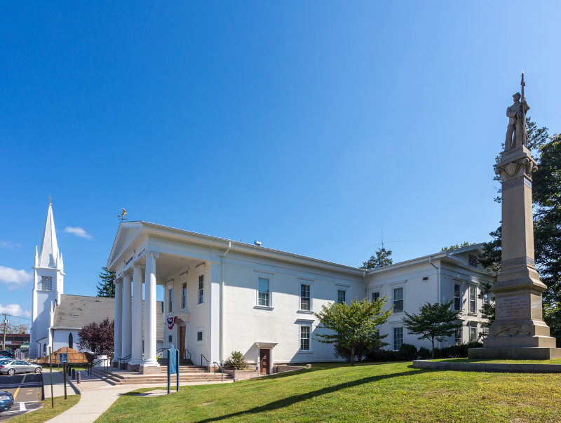 Historic white building with columns and a tall stone monument under a clear blue sky