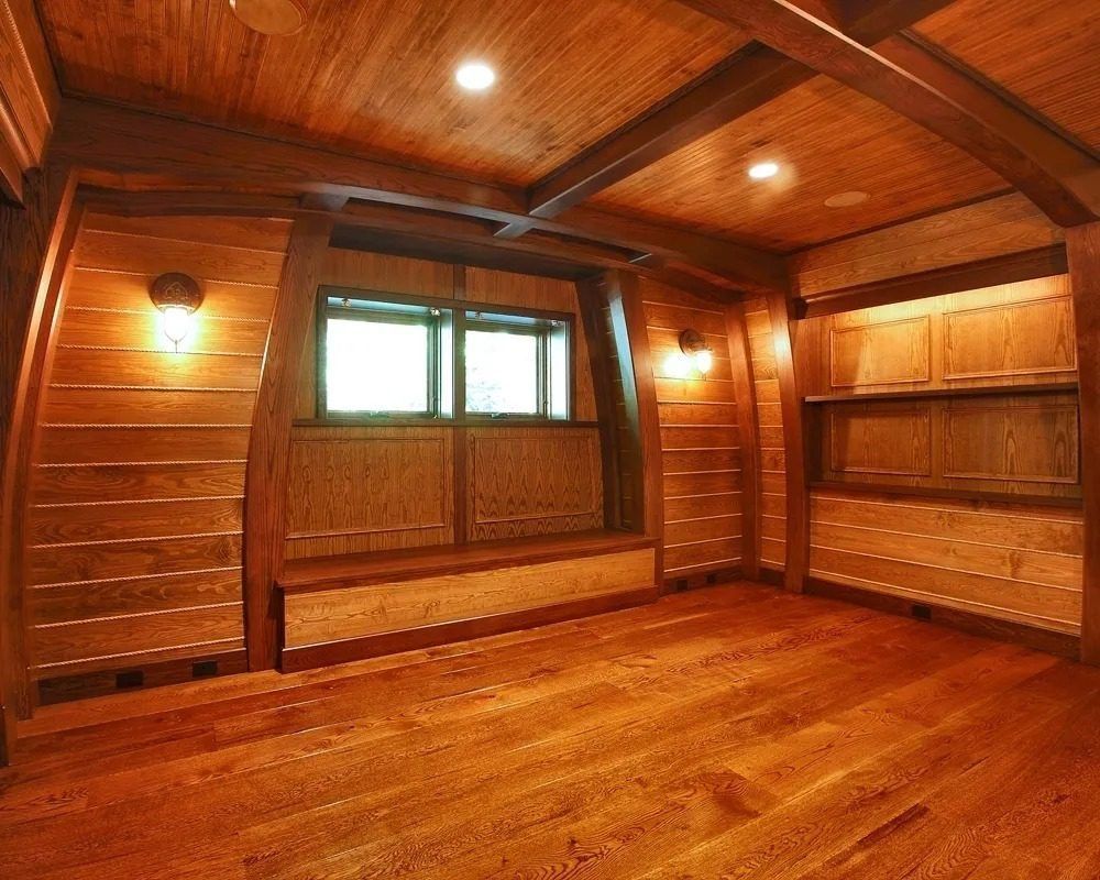 Empty wood-paneled room with vaulted ceiling, built-in bench, window, and warm wall sconces